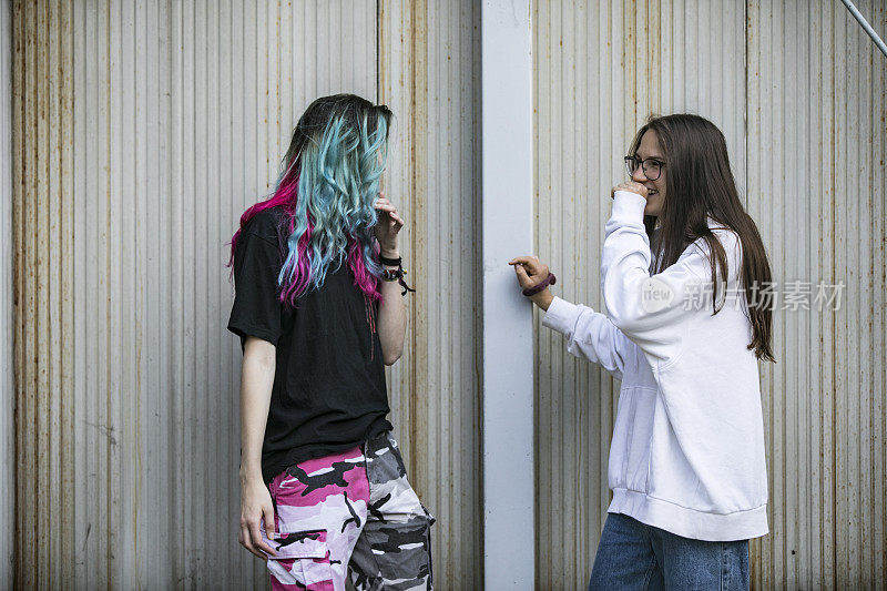 两个女朋友在玩，站在破烂的金属墙前