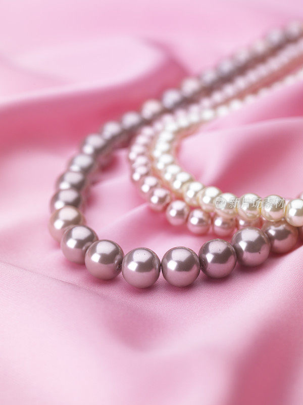 彩色珍珠项链在粉红色丝绸面料的背景。