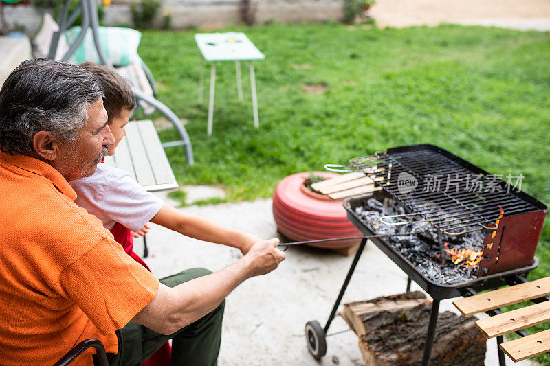 祖父和孙子用火熨斗戳烧烤时的木炭