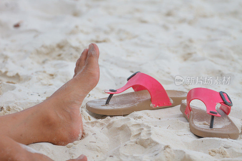 年轻女孩的腿和拖鞋在沙滩上