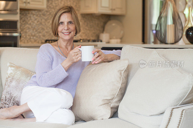 漂亮的老女人在沙发上享受她的茶