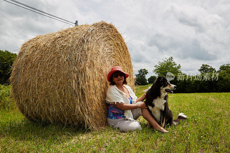 成熟的西班牙女人和狗放松在干草捆上
