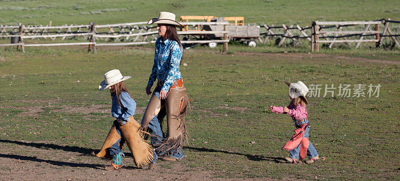 西部女牛仔妈妈和女儿们在篱笆旁走着