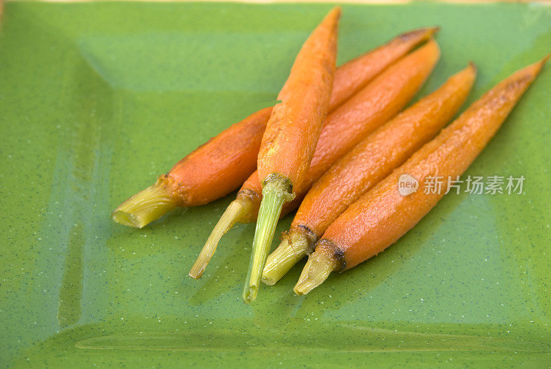 小胡萝卜在绿色盘子，煮新鲜烤蔬菜背景