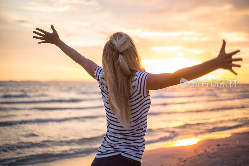 欢呼的女人在海边向夕阳张开双臂