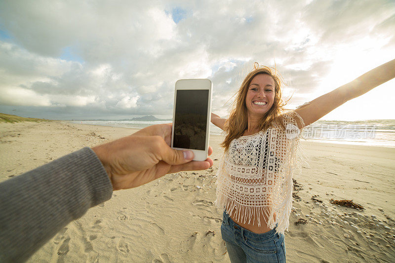 日落时分，一名男子在海滩上给一名女子拍照