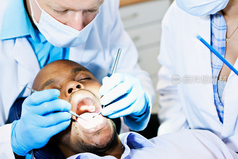 牙医兼助理忙着治疗一位斜倚的男性病人