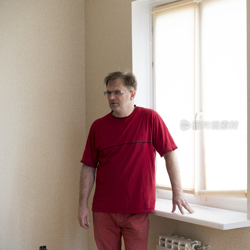 一个成熟的男人穿着红色的衣服在窗户旁边摆姿势
