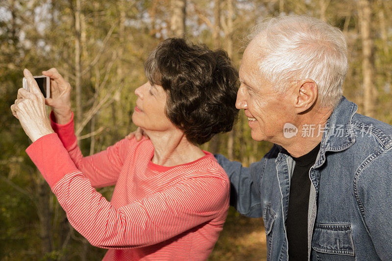 老年:活跃的老年夫妇在户外用智能手机拍照。