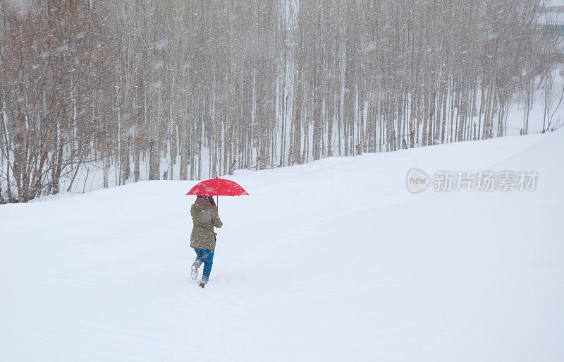 女人撑着红伞走在雪道上