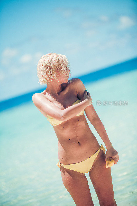 性感女人站在那里，为马尔代夫的日光浴涂抹奶油