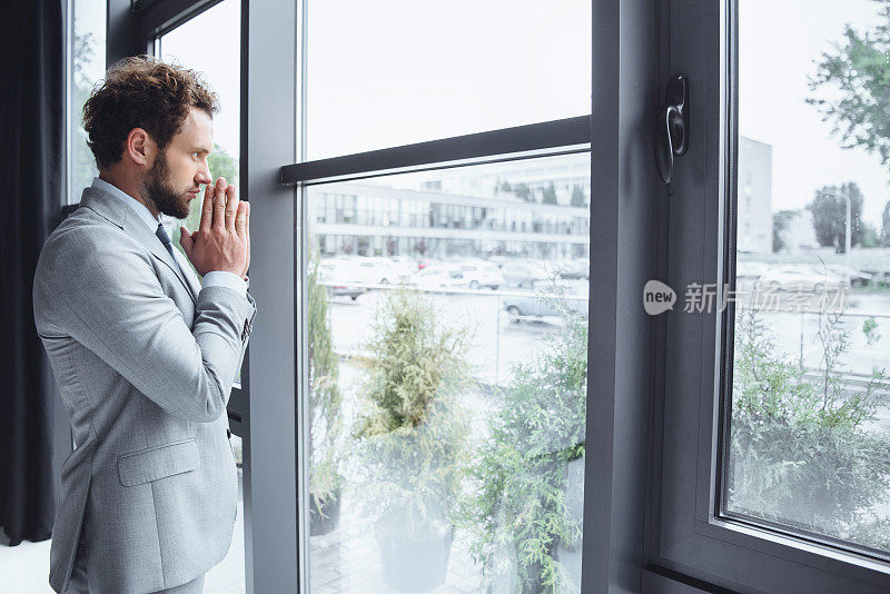 一幅白人商人站在办公室窗户前祈祷的肖像