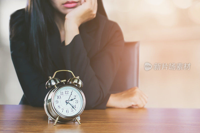 浪费时间的概念与亚洲商务女性感到疲倦和无聊的等待有人与办公桌上的闹钟ng时间概念与商务女性等待某人迟到看着桌子上的闹钟不高兴的脸