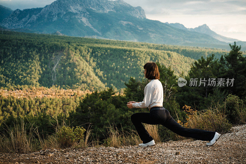 年轻的女性跑步者在晨跑前热身森林小径