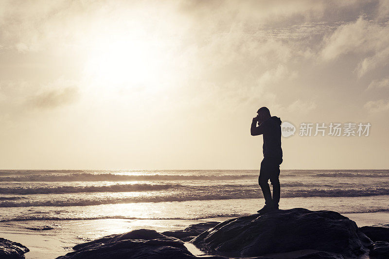 一名男子站在日落附近的水门湾海滩上拍照。