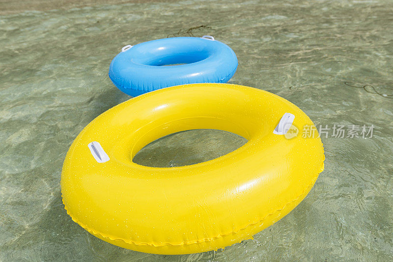 黄色和蓝色的橡胶圈漂浮在清澈的蓝色海洋上，康沃尔。
