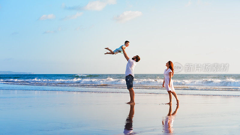 家庭-父亲，母亲，婴儿散步在日落海滩