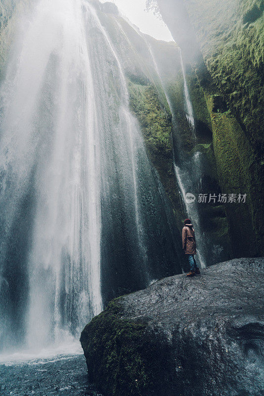 一个女人站在山洞里瀑布附近的岩石上