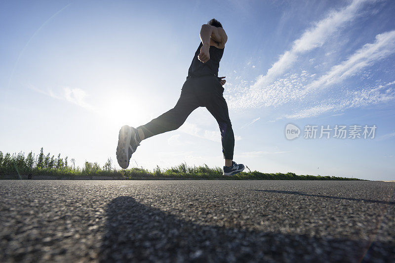 年轻的男运动员在柏油路上迎着天空奔跑