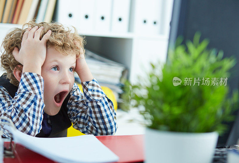 一个卷毛的白人小男孩抓住他的头，看着电脑屏幕。父母控制孩子上网的概念