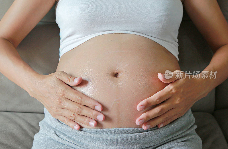 一位年轻的孕妇在肚子上擦药膏。