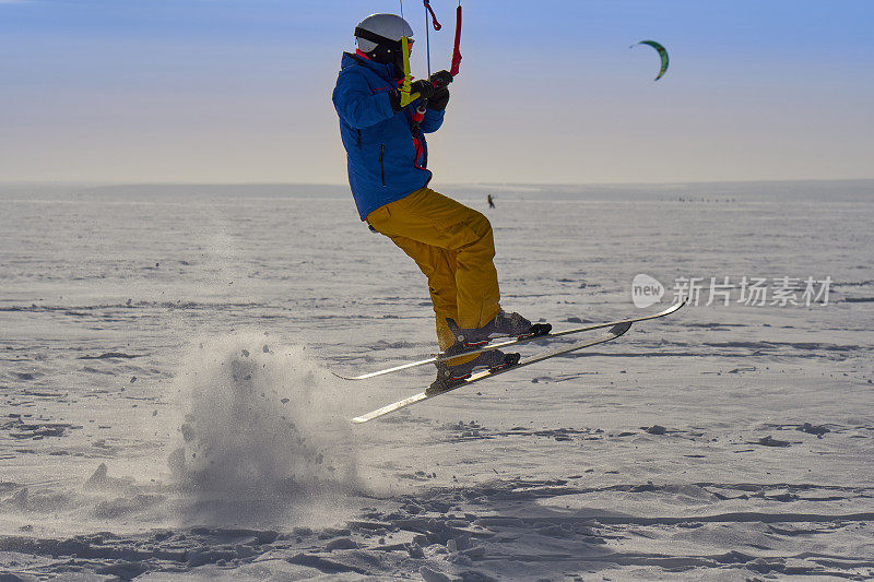 一个男运动员正在一个大的雪湖上的冰上放风筝。他跳起来。冬天晴朗有霜的一天。特写镜头。