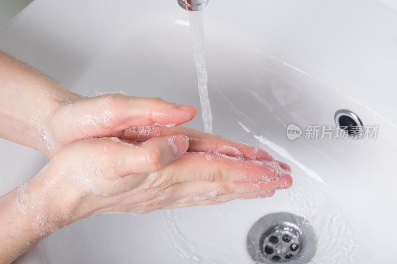 用肥皂在流动的水中洗手，在一个贝壳的浅色背景上