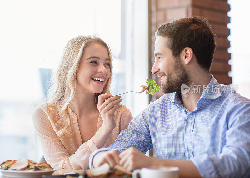 一对快乐的千禧夫妇在咖啡馆一起吃饭，年轻的女士给她的男朋友美味的沙拉