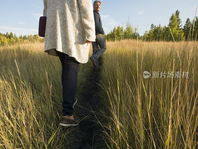 女人沿着一条狭窄的小路穿过高高的草丛走向男人