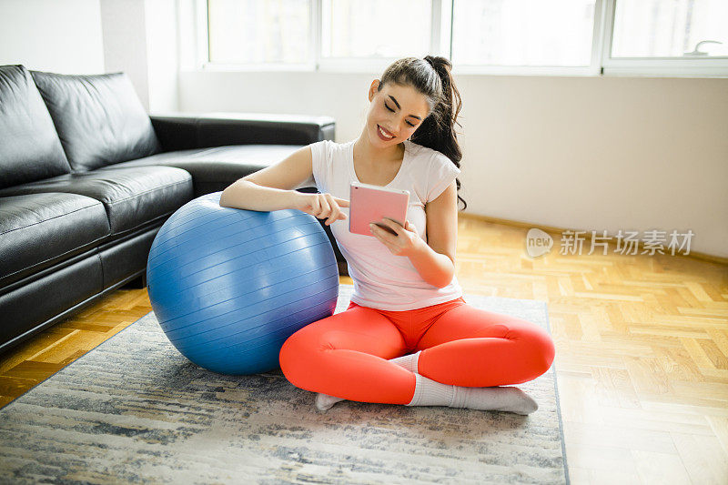 健身女性在家高强度锻炼后，在平板电脑上阅读在线体育杂志