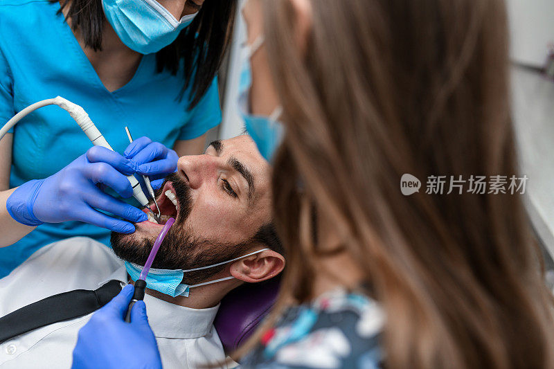 当牙医在给一个年轻人钻孔时，他坐在牙科椅上。