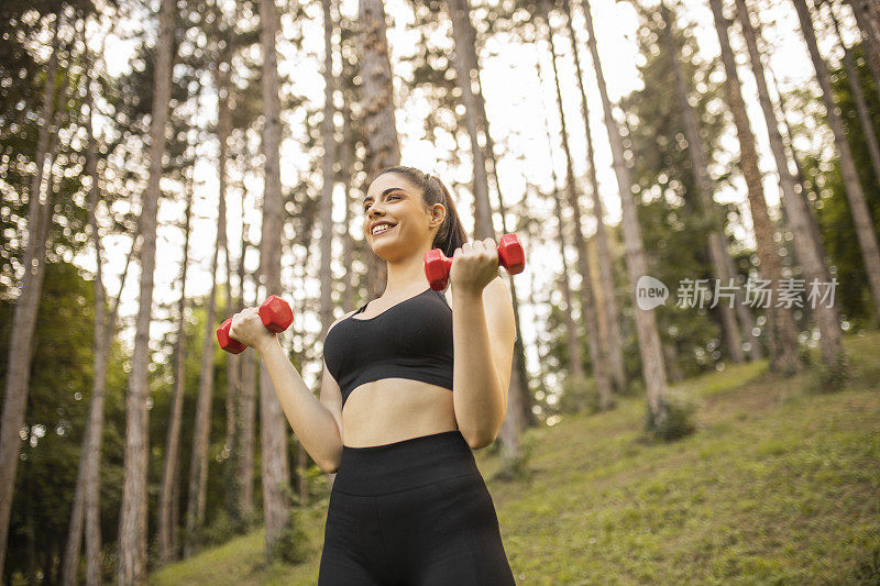 一幅美丽的年轻女子在户外举哑铃的肖像