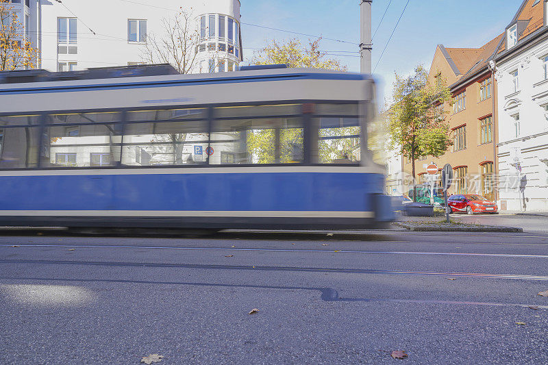 模糊的蓝白有轨电车在一个城市设置与汽车，树木和秋叶