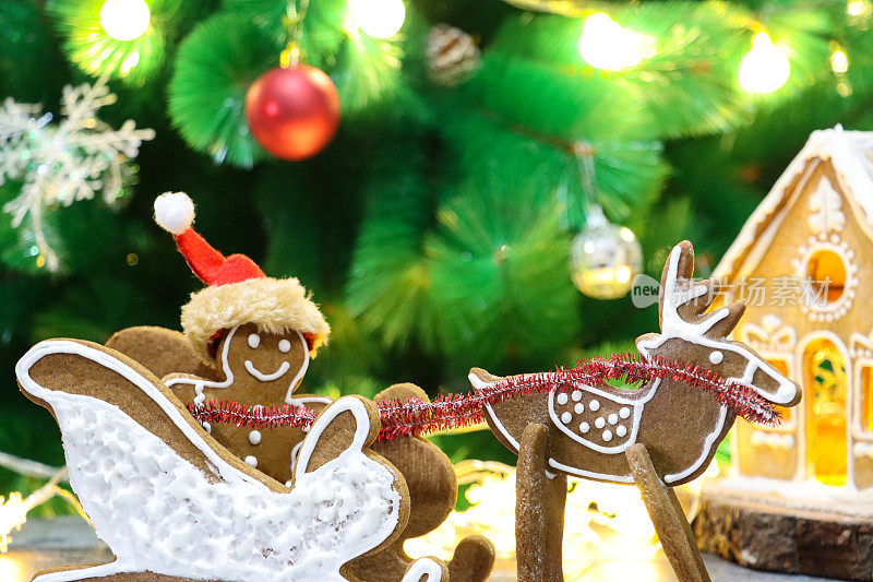 自制的姜饼饼干圣诞老人、驯鹿和雪橇、用白色皇家糖衣装饰的姜饼屋展示在客厅里，前面是一棵覆盖着小玩意和发光的仙女灯的圣诞树，集中在前景上