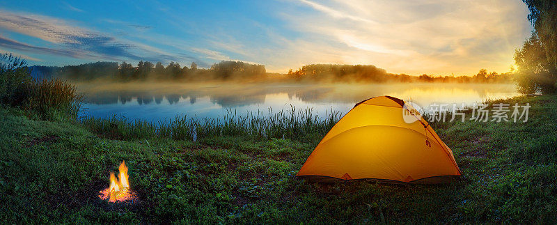 黄昏时分，雾蒙蒙的河边，橙色的帐篷和篝火