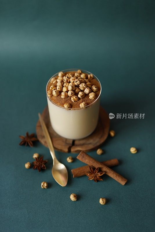 传统土耳其甜点“Boza”，装在玻璃杯里，木制的杯垫上，背景为蓝绿色