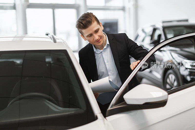 年轻英俊的汽车销售员在经销商中心检查汽车销售