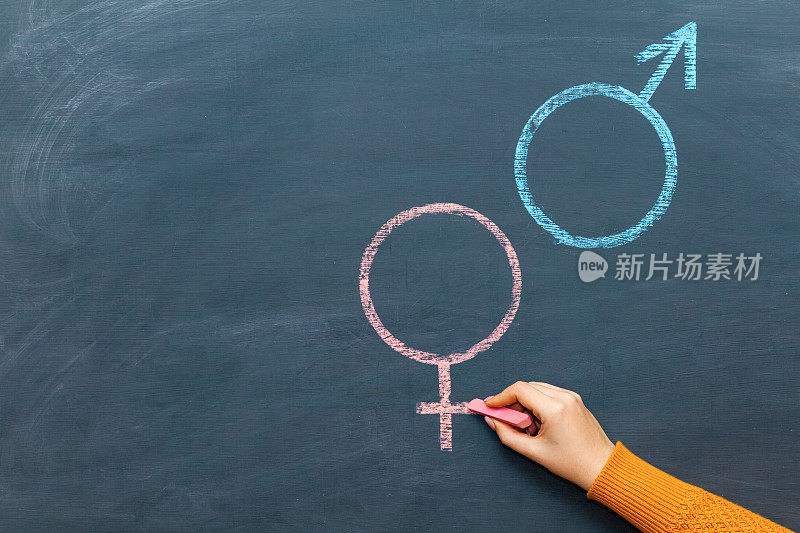 一个女人用粉笔在黑板上画了一个男性和女性的性别符号，性别平等和同工同酬的概念。本空间