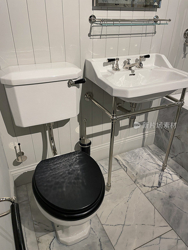 白色和灰色大理石地砖的豪华浴室套房，白色陶瓷浴缸，水池，WC厕所，不锈钢维多利亚式龙头和淋浴水管的卫生间，木制面板墙