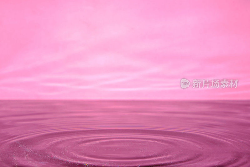 明亮的粉红色背景与发散的圆圈从水滴表面的水。