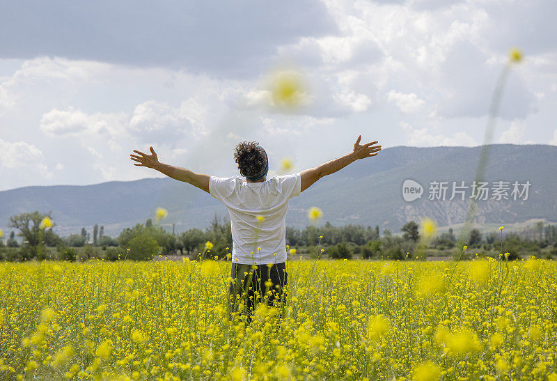 一个年轻人的后视图享受自然草地上的野花在日落