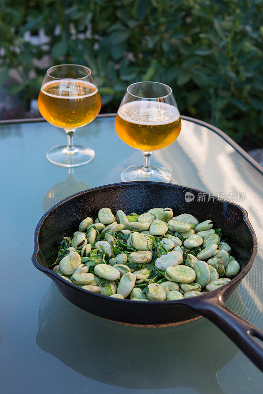 新鲜的蚕豆，用橄榄油煎过，放在1940年代的古董铸铁锅上，摆在蚕豆植株前