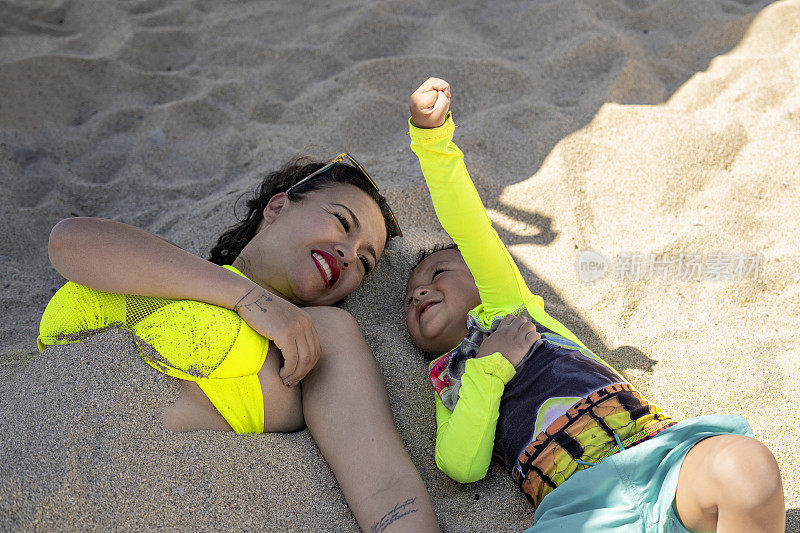 母亲和儿子躺在沙滩上快乐地享受着假期中最美好的时光。