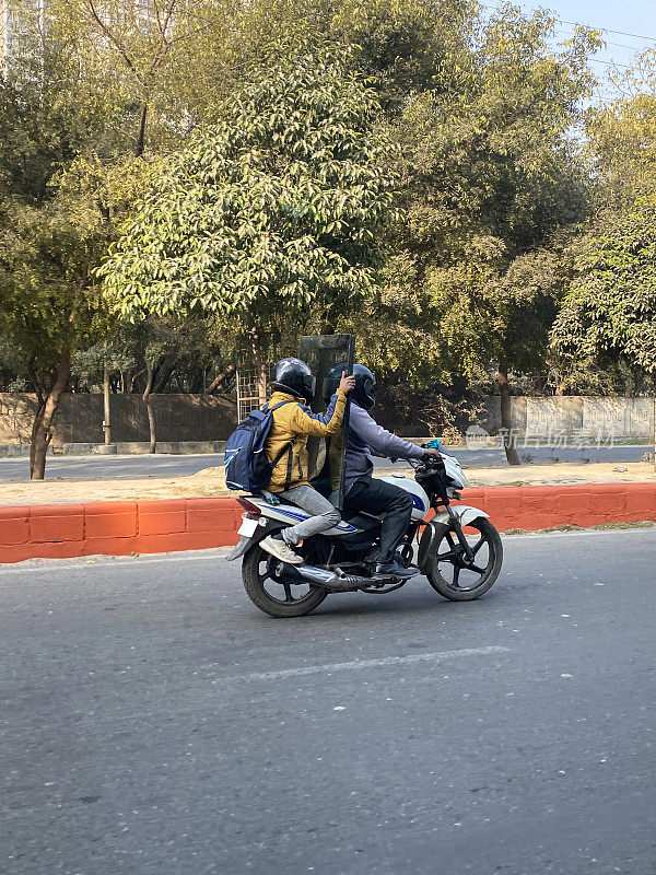 特写，两名戴安全帽的摩托车在居民区的道路上行驶，背着背包的乘客背着大包裹，危险驾驶，聚焦前景