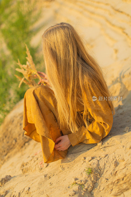 自然美景。穿黄色衣服的金发女人躺在河岸上。夕阳的光。夏天的一天。长头发的。沙子。