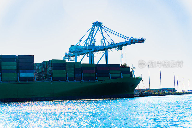 停靠在繁忙的洛杉矶港口的巨型货船创造了令人印象深刻的景象。随着起重机装卸集装箱，它们巨大的船体隐约出现在水面上，促进了全球贸易和经济交流。