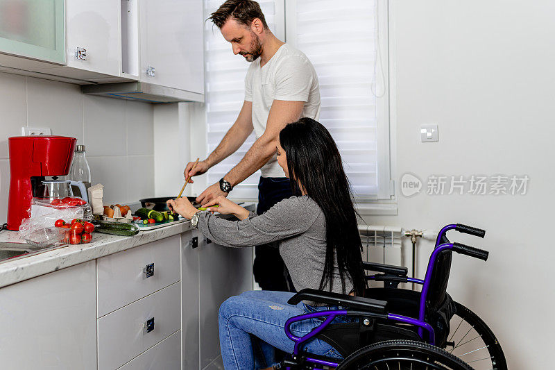 坐在轮椅上的妇女在厨房得到她的伴侣的帮助