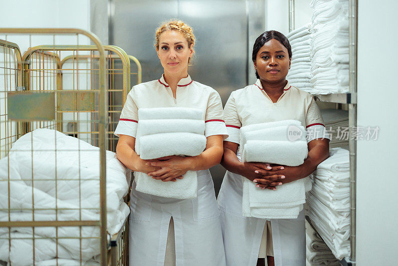 非裔美国人和白人酒店的女服务员拿着干净的毛巾站在一起洗衣服