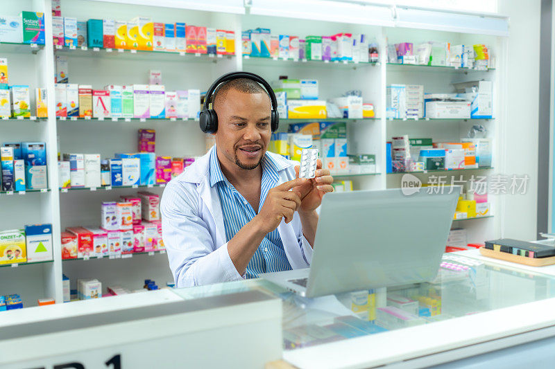专业拉丁中年药师戴着耳机，穿着白大褂，用电脑直播，在线销售药包。非洲中年成年推销员在药店向网上顾客推荐药品。