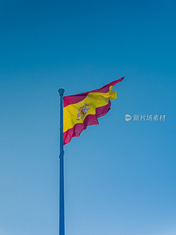 旗杆上插着西班牙国旗迎风飘扬，以蓝天为背景，复制空间